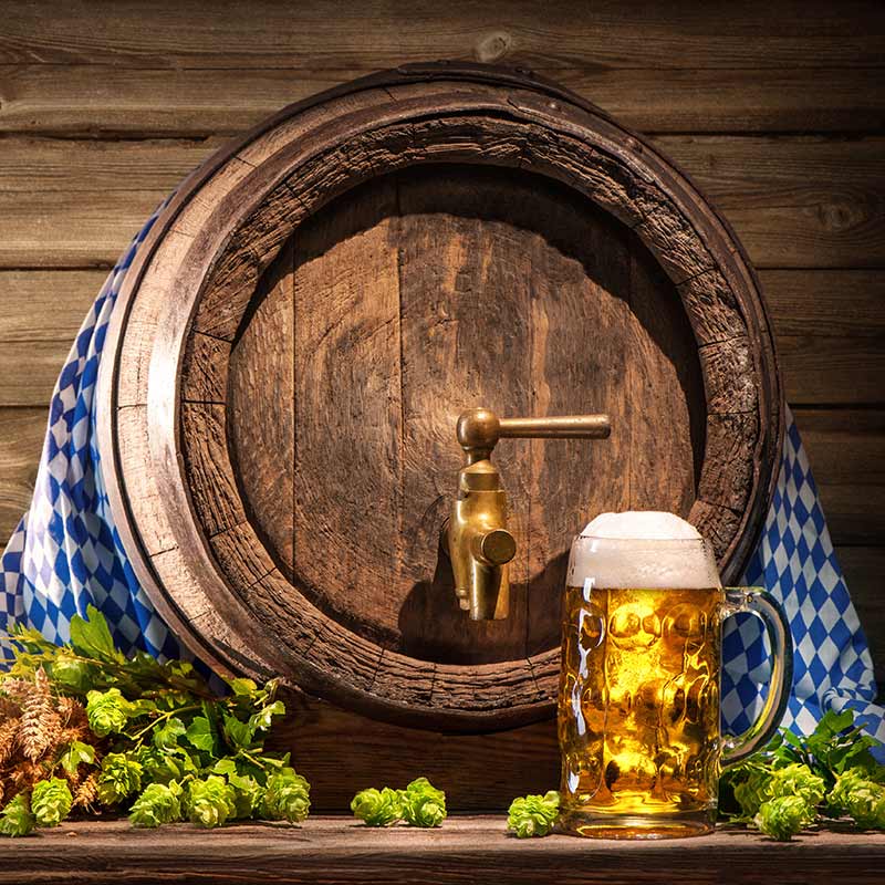 Frisch gezapftes Bier vom Fass vor rustikalem Holzfass mit Hopfen und bayerischem Tuch – Biergenuss im Restaurant Storchennest Bensheim